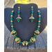 Emerald and gold necklace and earrings in the shade. Deep emerald green beads and bright gold components against the black jewelry display.